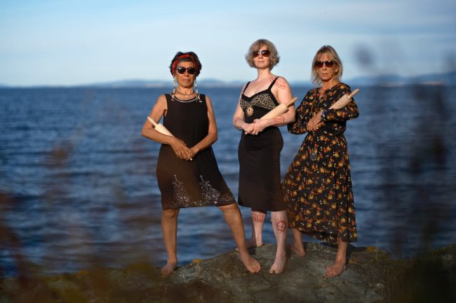 Tre kvinner står ved havet.