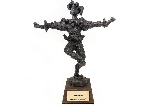 Bilde av statuetten narren som eræresprisen. det er en bronsefigur av en narr som står på ett be og med armene ut